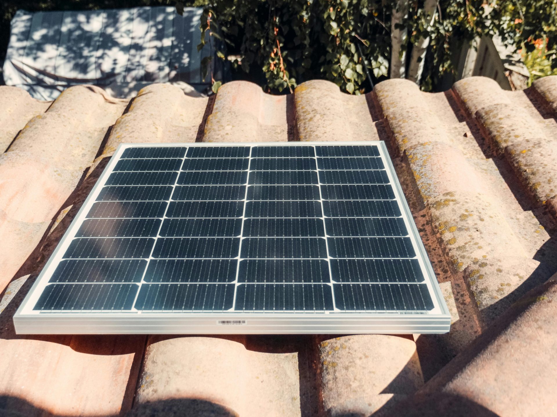 Ein einzelnes Solarpanel auf einem rustikalen Ziegeldach, das in der Sonne glänzt. Umweltfreundliche Energie.